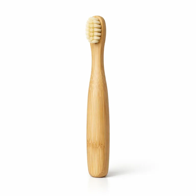 A highly detailed photo of a bamboo kids toothbrush in a natural light wood finish, featuring gently rounded edges for added kid safety and comfort. The child-sized handle and soft bristles are designed for young children.